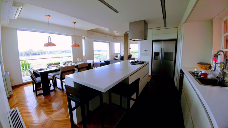Diseño interior y reforma de arquitectura, cocina abierta, integrada o americana, en corian blanco, detalles en acero inox y lamparas de cobre